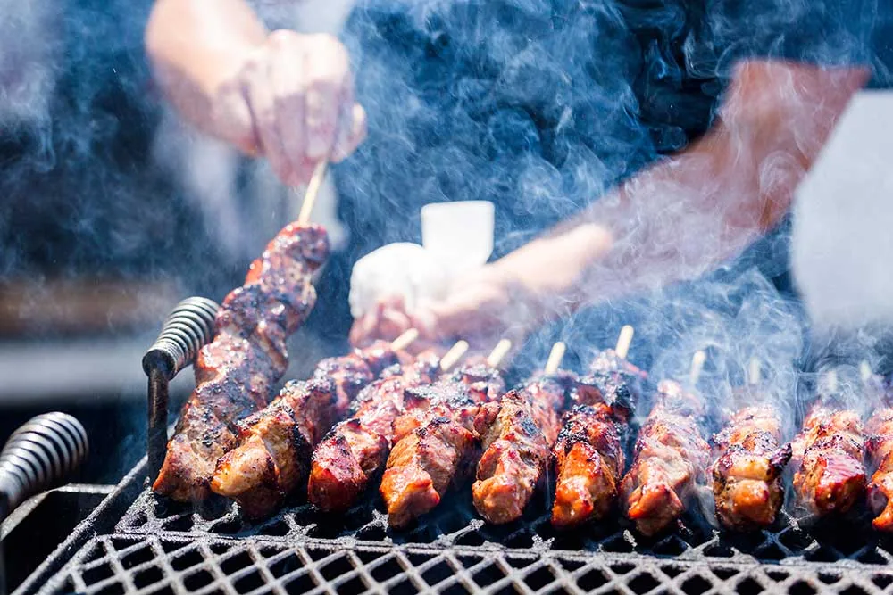 Racks of ribs slow-smoking over coals on a barbecue grill.